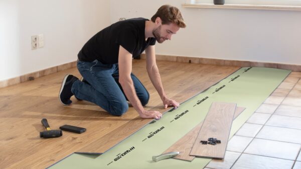 A man kneeling on the floor, measuring and installing vinyl flooring planks.